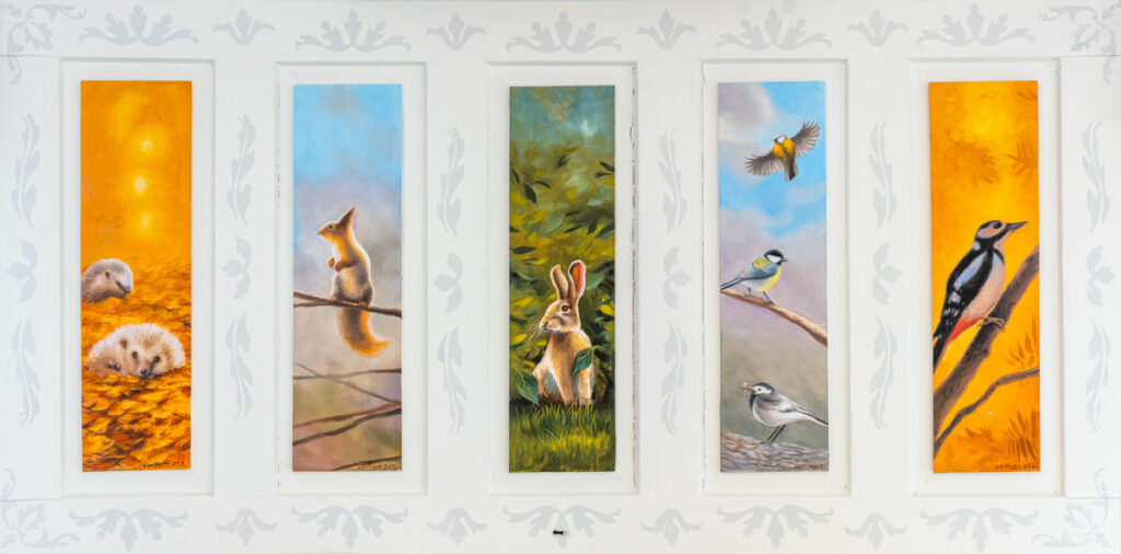 Viisi pystysuuntaista maalauspaneelia, joissa on eri vuodenaikojen tunnelmia ja suomalaisia metsäneläimiä: vasemmalta siilit syksyisillä lehdillä, orava kevätaamun valossa, jänis kesäisessä vihreydessä, kolme lintua oksilla sinistä taivasta vasten ja tikka syksyisellä oksalla. Taustana vaalea koristeellinen seinäpinta.